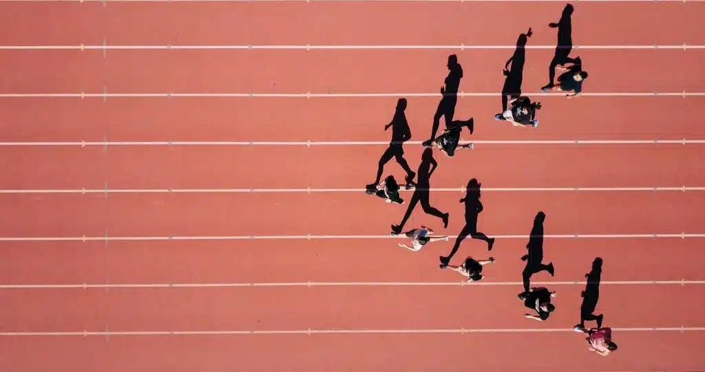 Vertriebserfolg trainieren wie Profisport: Das Bild zeigt Läufer auf einer Laufbahn aus der Vogelperspektive. Jeder Athlet verfolgt sein eigenes Tempo und Ziel – genau wie erfolgreiche Vertriebsteams, die mit Disziplin, Ausdauer und kontinuierlichem Training Spitzenleistungen erreichen. Die roten Bahnen symbolisieren klare Prozesse, strategische Planung und den Fokus auf messbare Ergebnisse im Vertrieb. Wer seinen Vertriebserfolg trainieren wie Profisportler möchte, setzt auf regelmäßiges Coaching, Leistungsanalysen und konsequente Weiterentwicklung statt auf kurzfristige Erfolge.