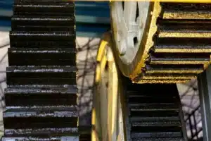 Zwei große, mit Schmierfett bedeckte Zahnräder greifen in einer Maschine ineinander.